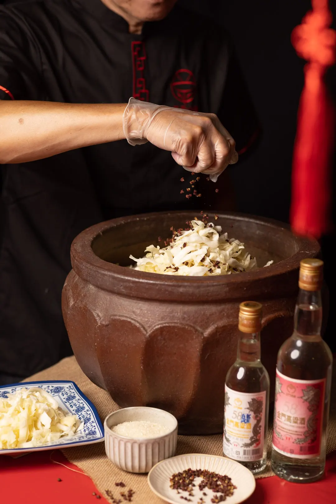 師傅把花椒撒進大缸，一層層醃酸菜，桌上擺著金門高粱酒