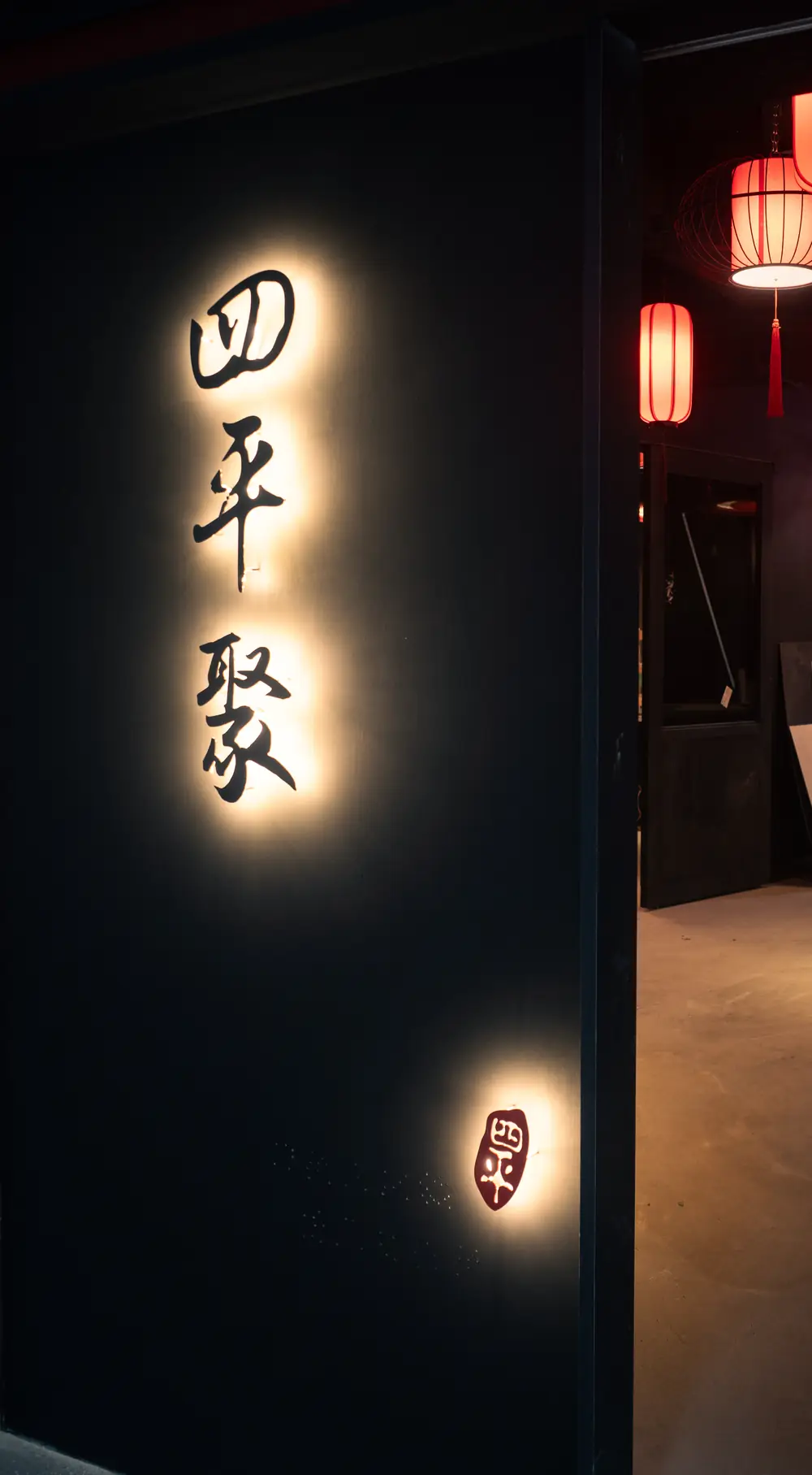 四平聚入口:深色牆面上背光的「四平聚」題字